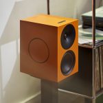 Cambridge Audio L/R X in Orange auf einem Standfuß neben einem Regal mit Schallplatten