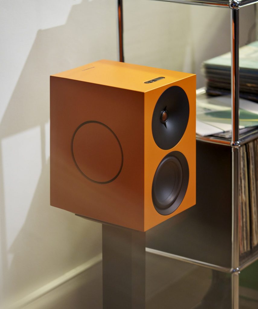 Cambridge Audio L/R X in Orange auf einem Standfuß neben einem Regal mit Schallplatten