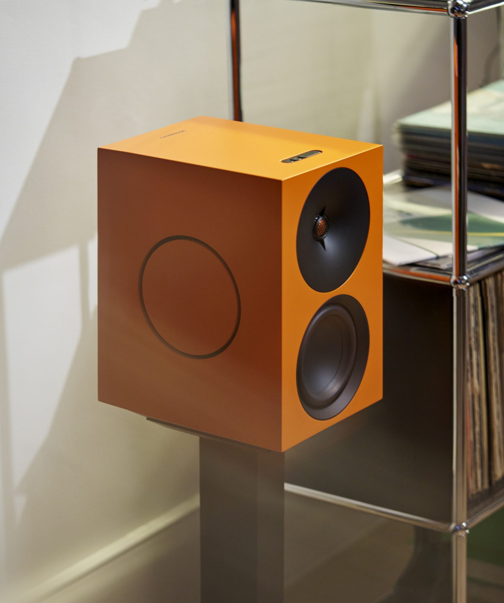Cambridge Audio L/R X in Orange auf einem Standfuß neben einem Regal mit Schallplatten